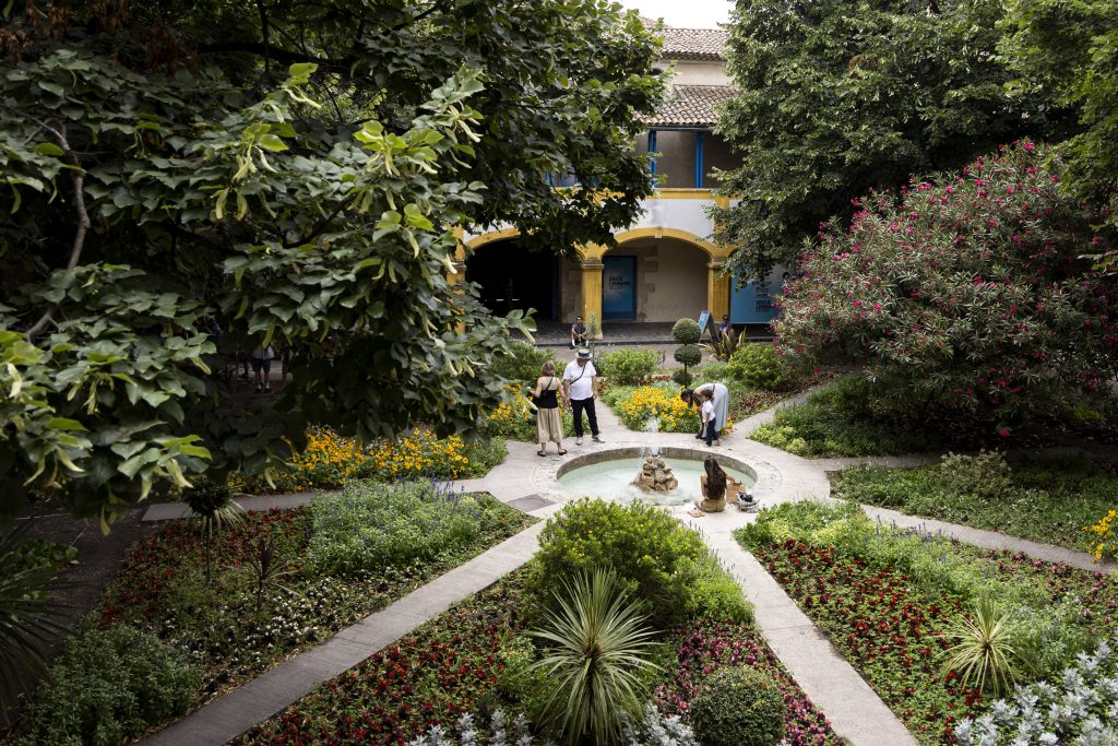 People stand in a garden with a fountain and colorful flowers.