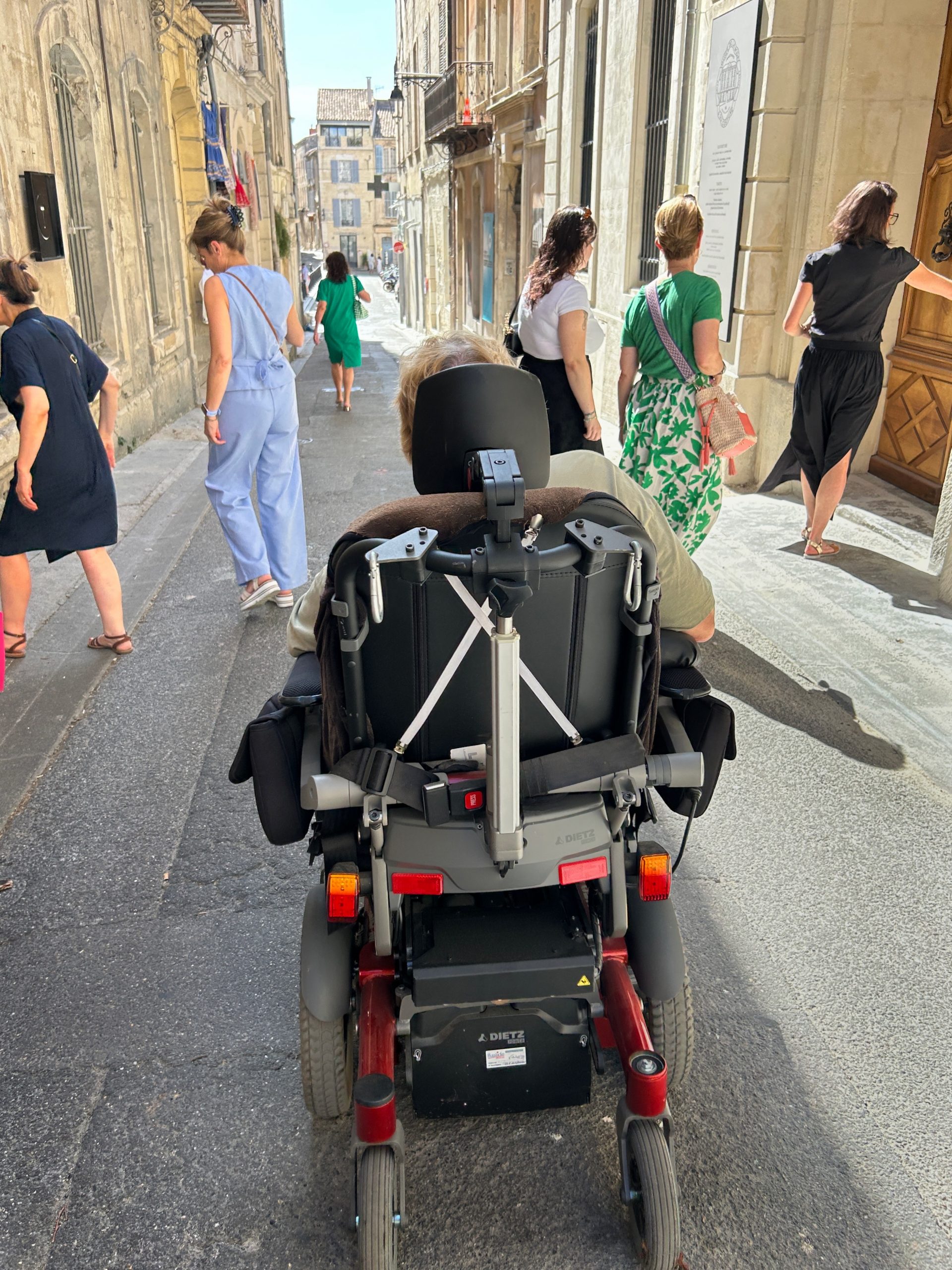 Person in a wheelchair shown from the back navigating a narrow street crowded with people walking.