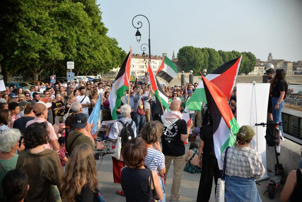 Demonstrators holding signs and Palestinian flags are shown protesting.