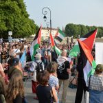 Demonstrators holding signs and Palestinian flags are shown protesting.
