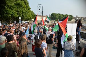 Demonstrators holding signs and Palestinian flags are shown protesting.