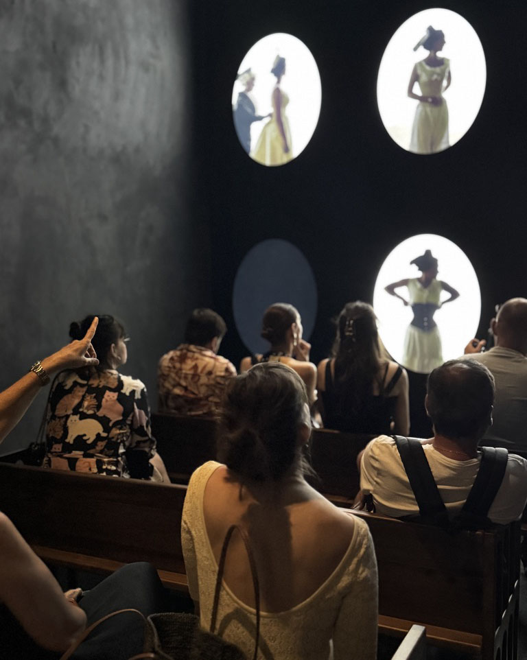 An audience watches a video presentation with silhouhettes of women in 18th century costumes portrayed in small circles.