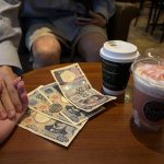 Money on a cafe table, with drinks. Two hands clapsed