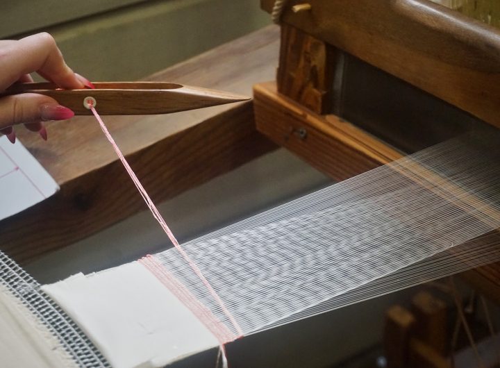 A wooden shuttle carries pale pink thread across the loom, adding another line to a piece of handwoven cloth. Photo by Katherine Istomin