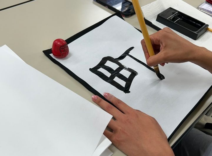 A hand writes a character in Japanese calligraphy
