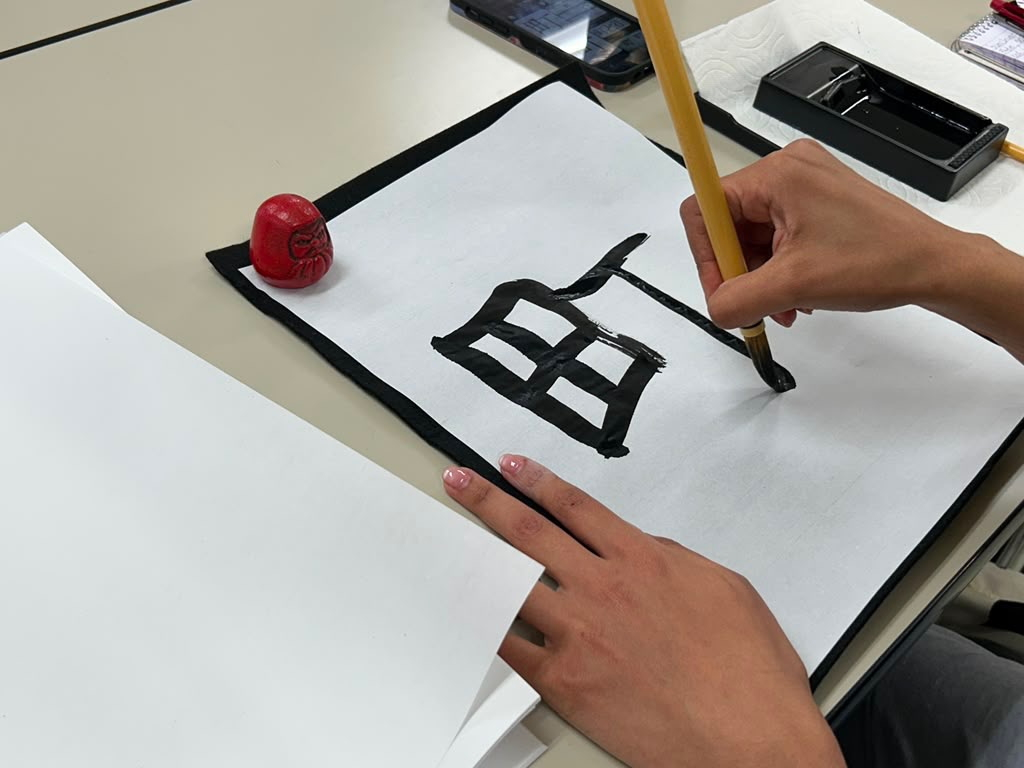 A hand writes a character in Japanese calligraphy